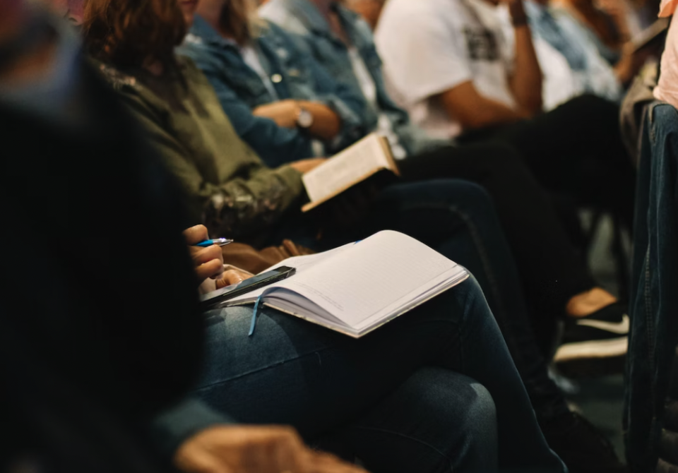 Room of people holding notebooks, phones, and posture as if in training session