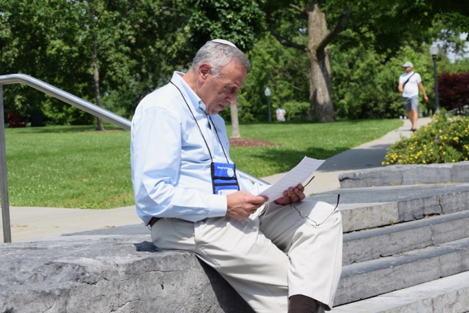Male Hebrew Lifelong Learner student sitting on steps outside of library, reading.