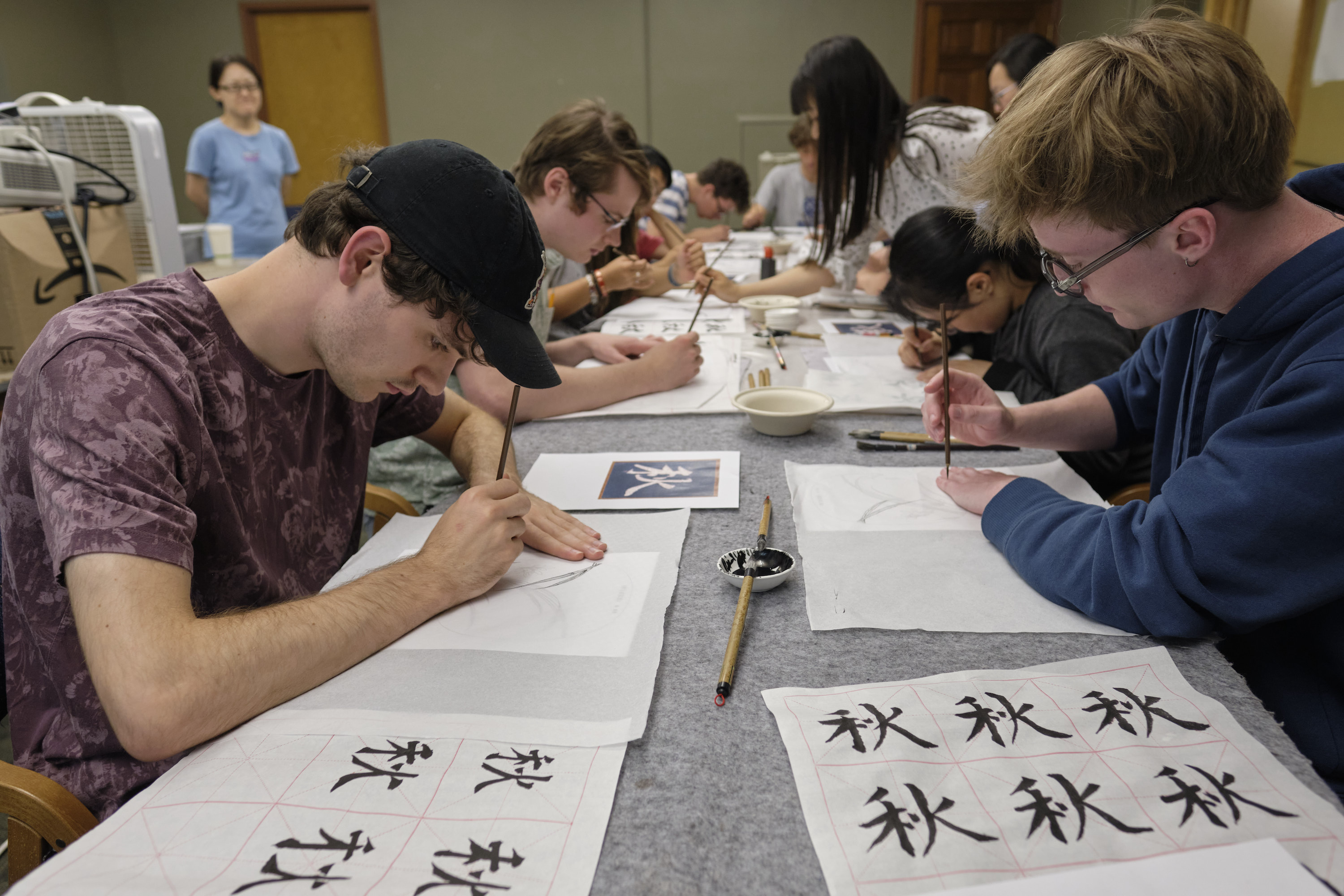 Students sit at a table practicing their calligraphy skills