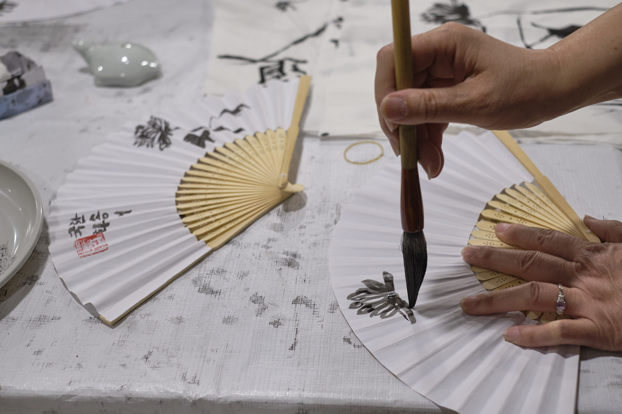 A woman's hand paints Korean calligraphy on a fan.