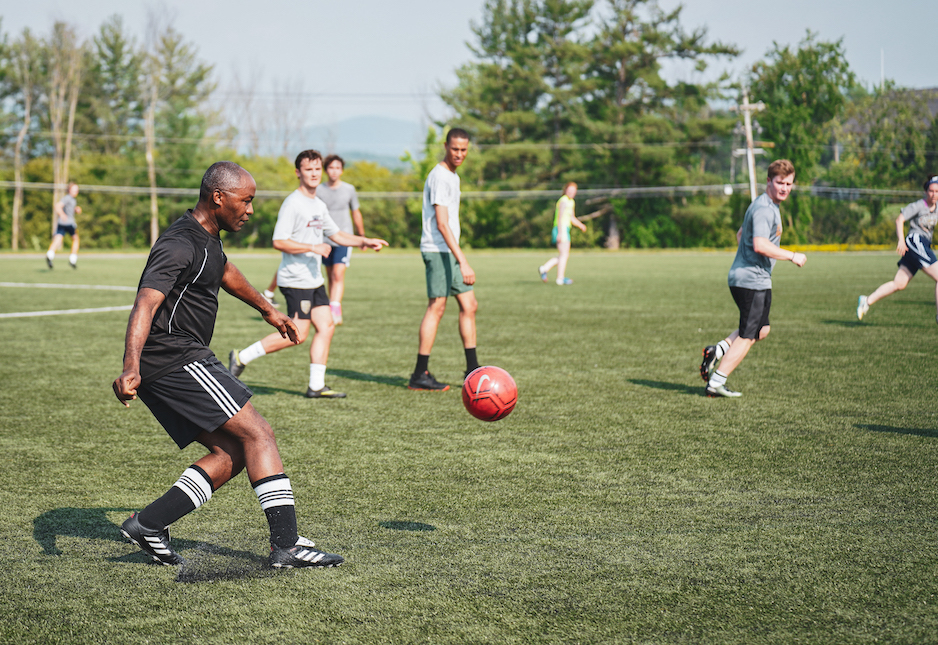 A group of men play soccer outside on a grass field.