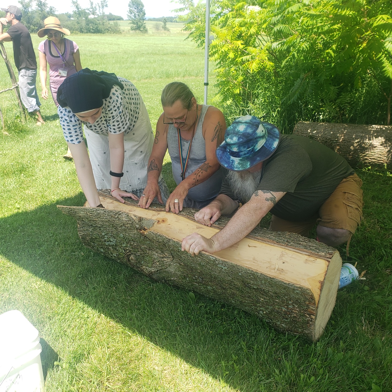 Students work to strip the bark off a log. 
