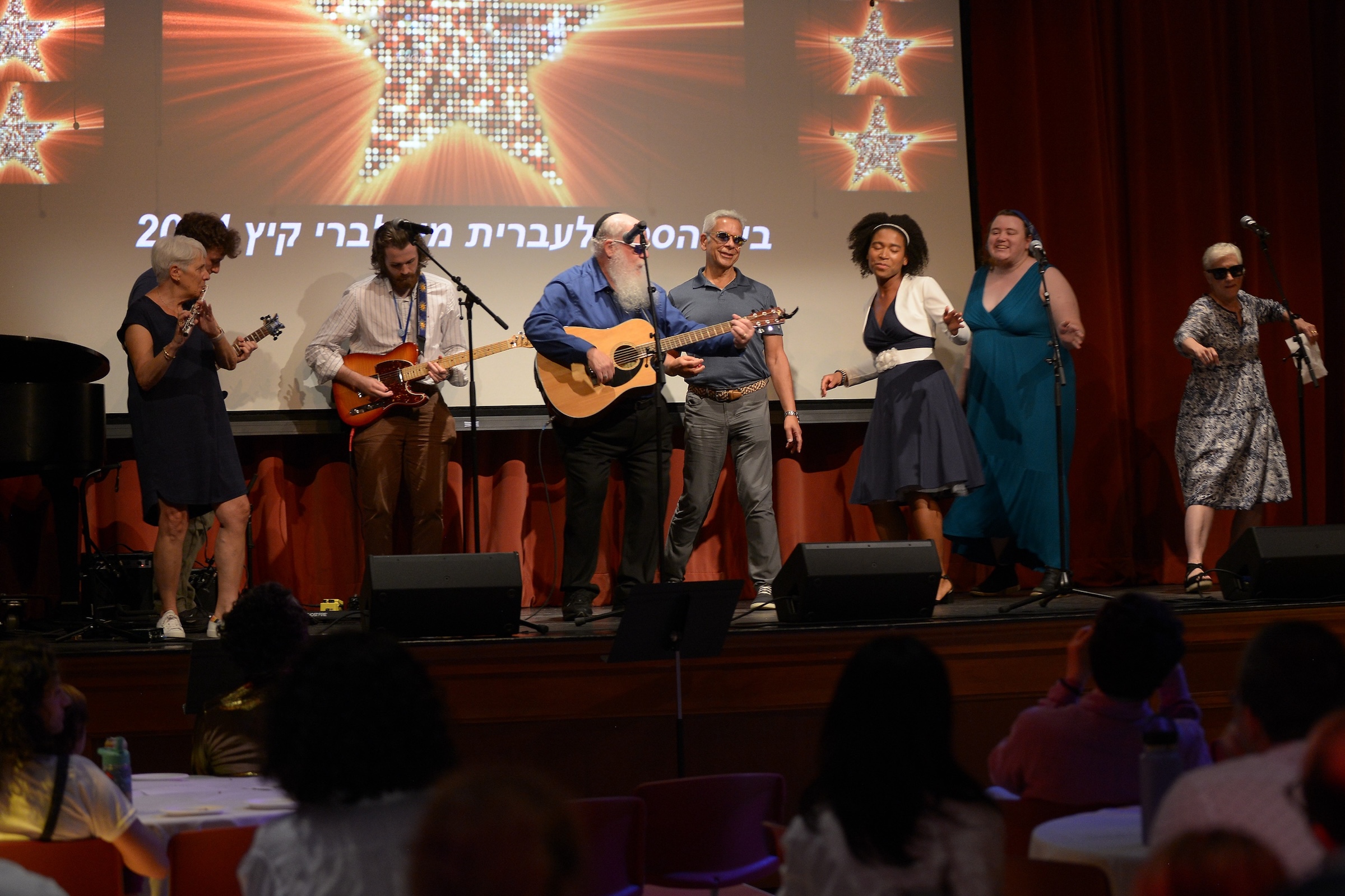 A group of musicians at the School of Hebrew sings on stage. 