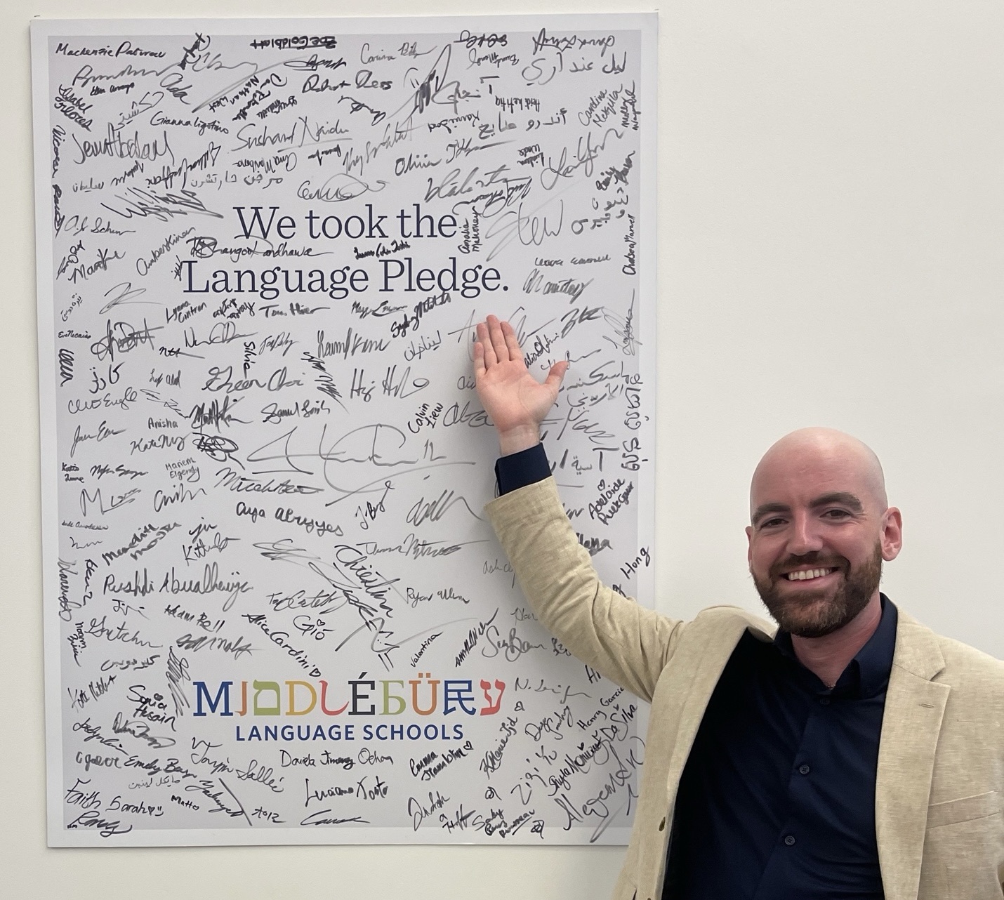 A man stands in front of a signed Language Pledge poster. 