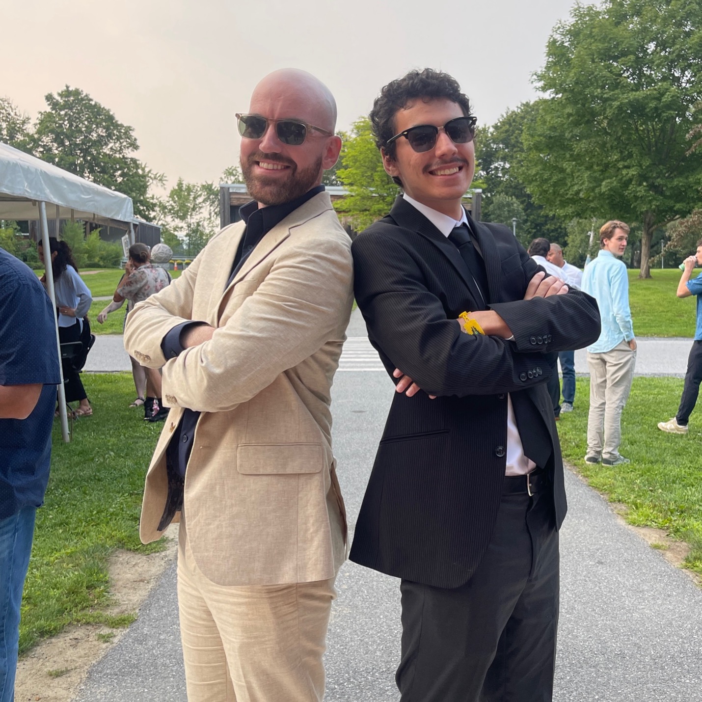 Two men in suits smile, back to back. 