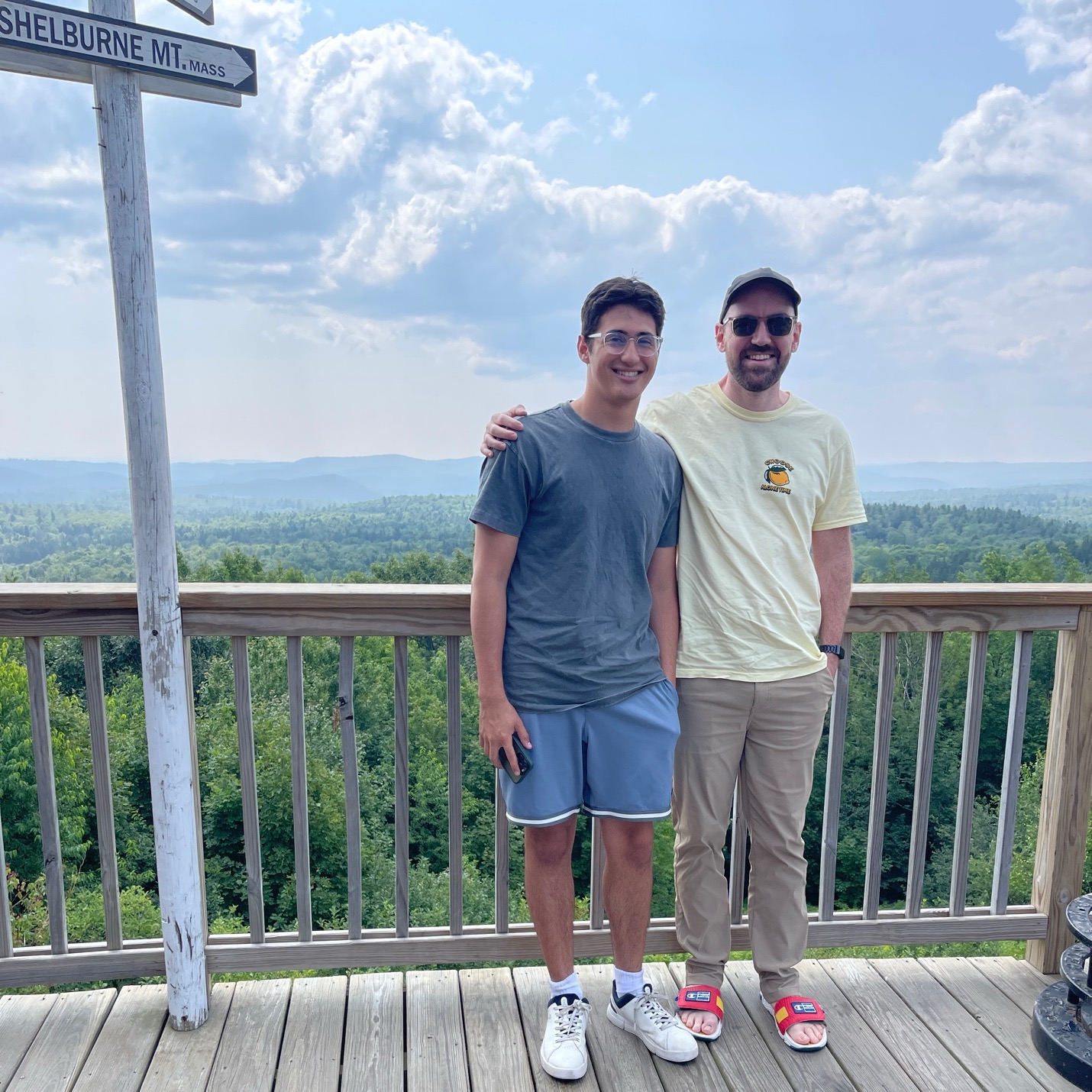 Two friends stand atop a deck with a view of the mountains. 