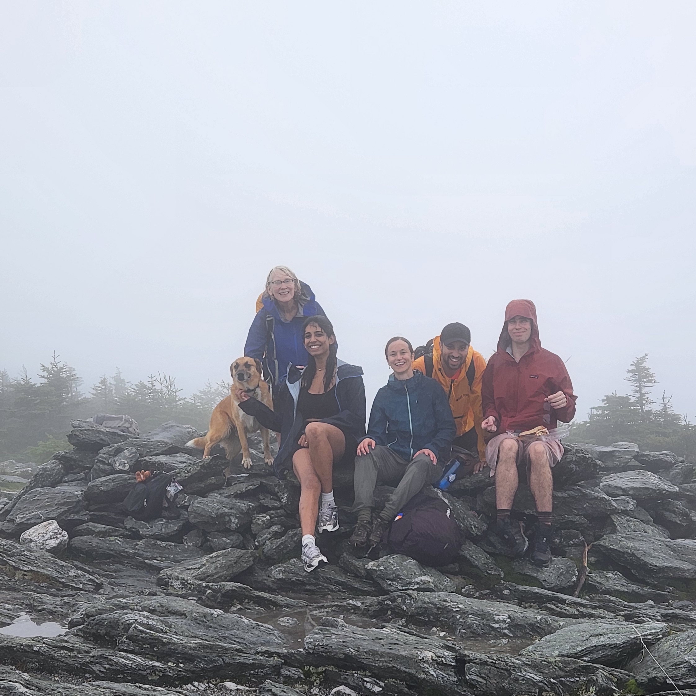 A group sits on a rock at the top of a rainy hike.