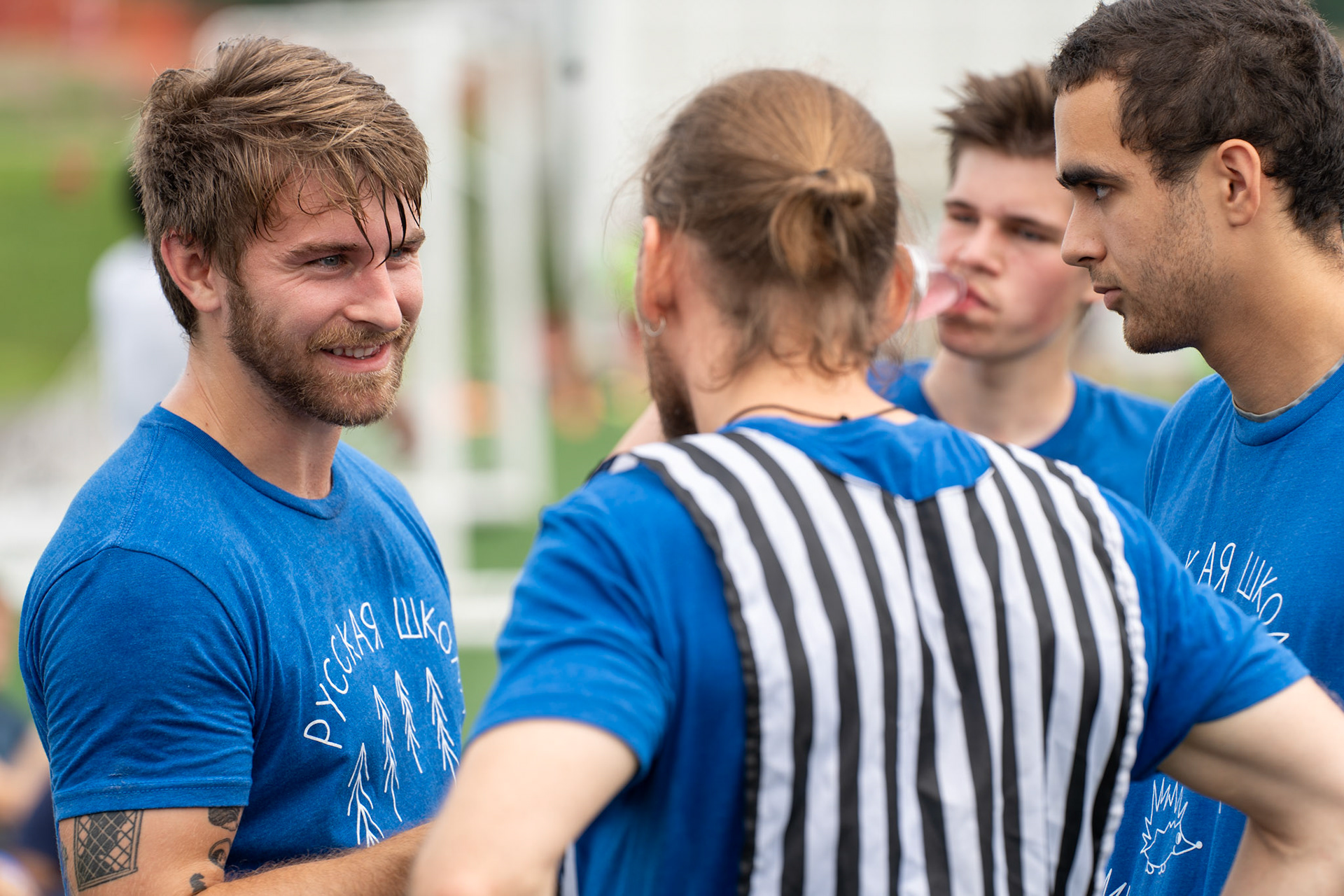 Two men in blue shirts chat on the soccer field. 