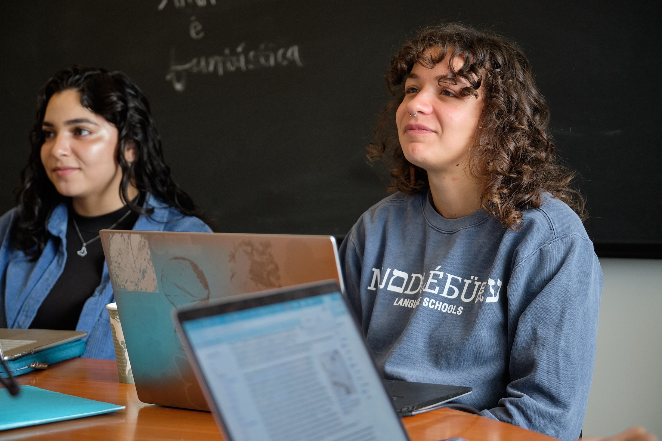 Two students sit smiling in Portuguese class. 