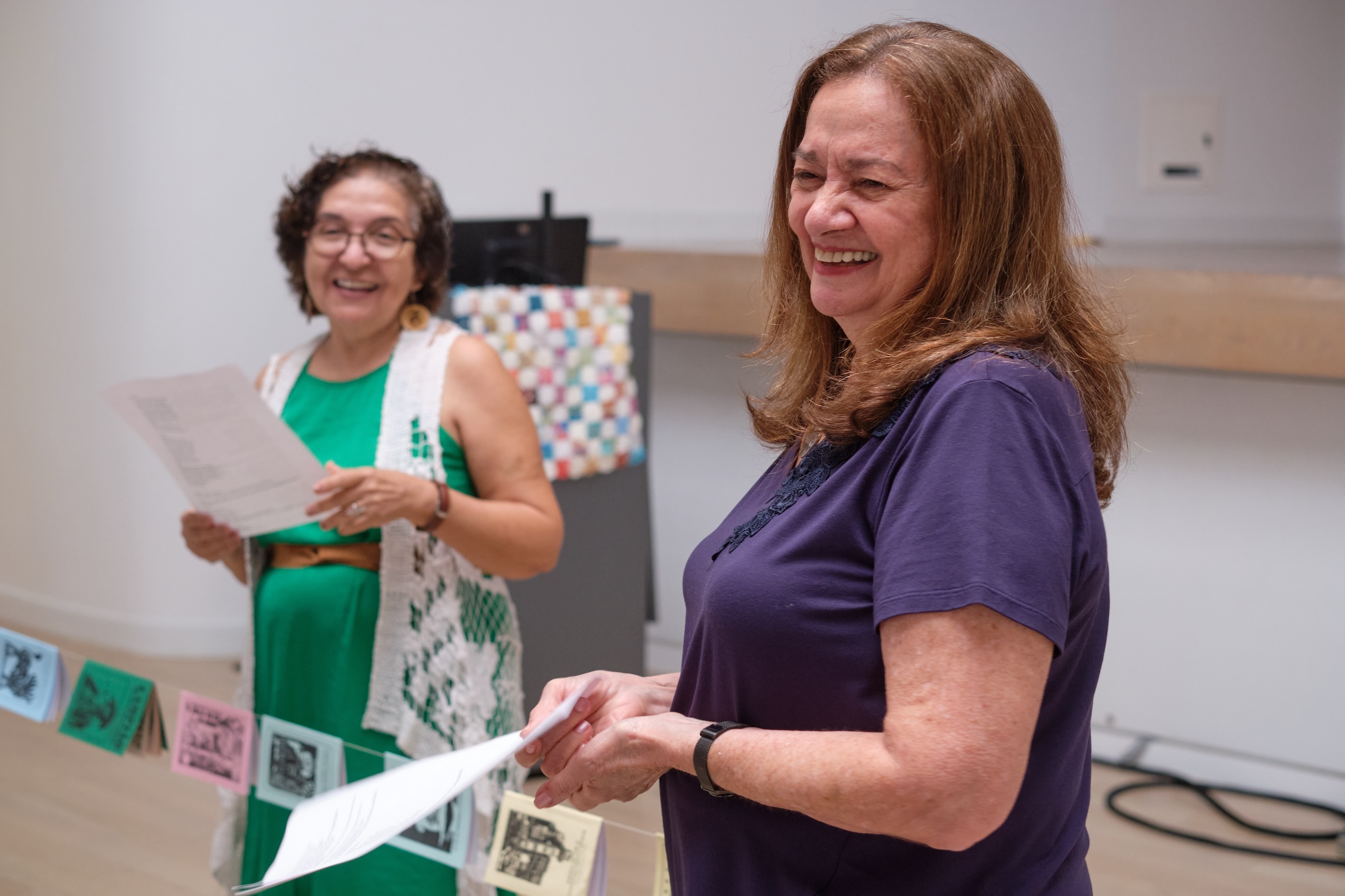 Two women smile with their scripts in their hands. 