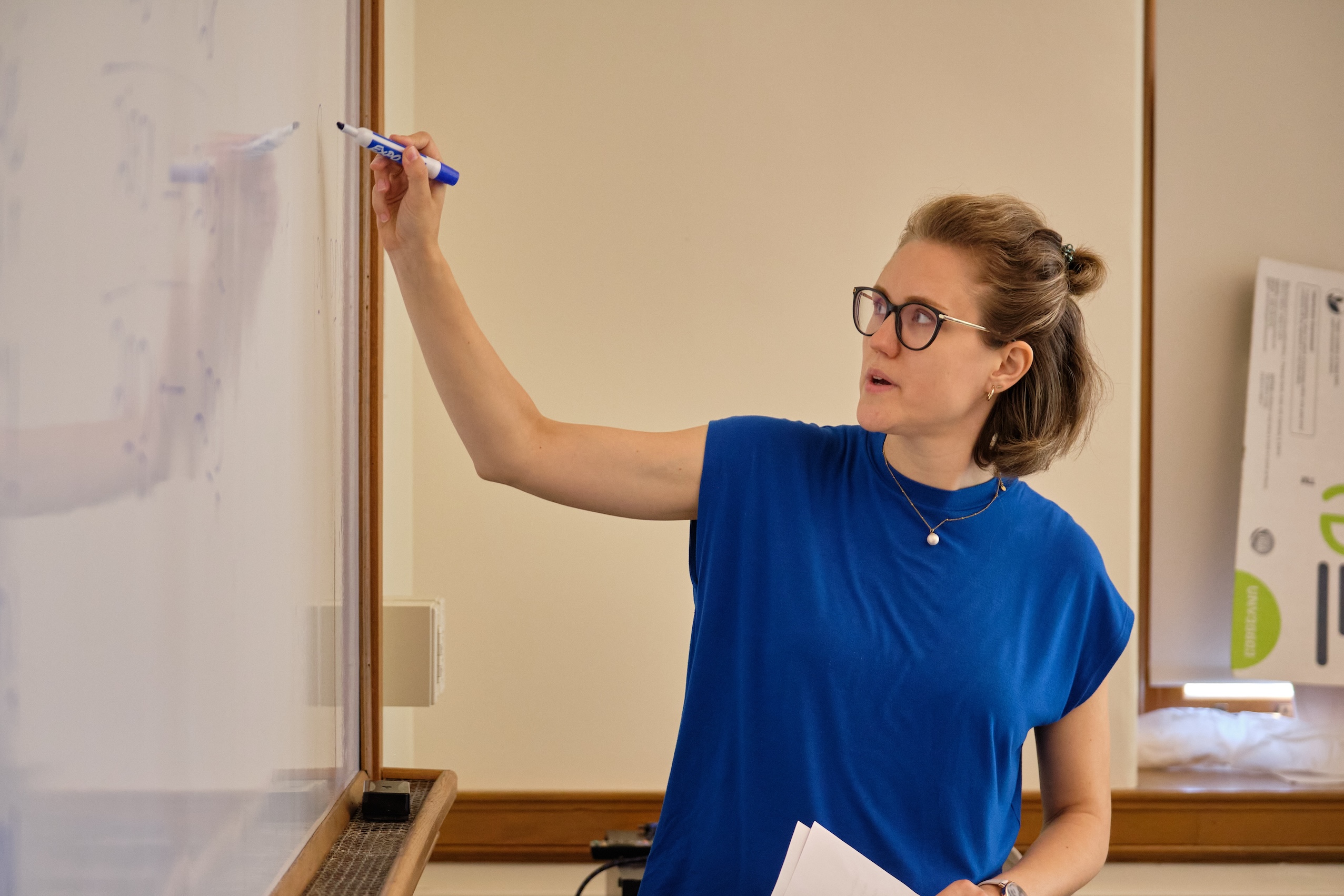 A teacher in a blue shirt writes on the whiteboard. 