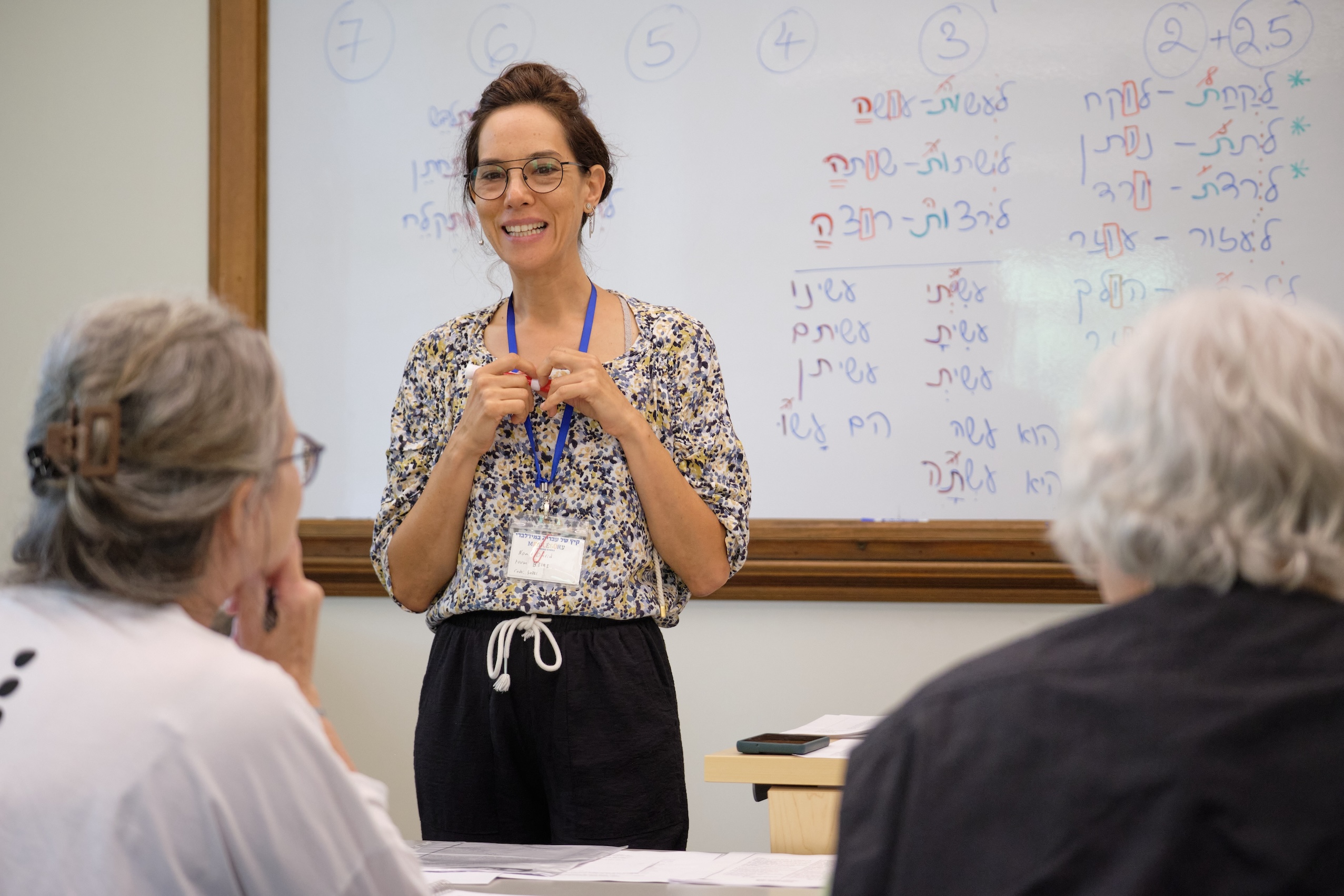 A teacher stands in front of a whiteboard with Hebrew writing on it. 