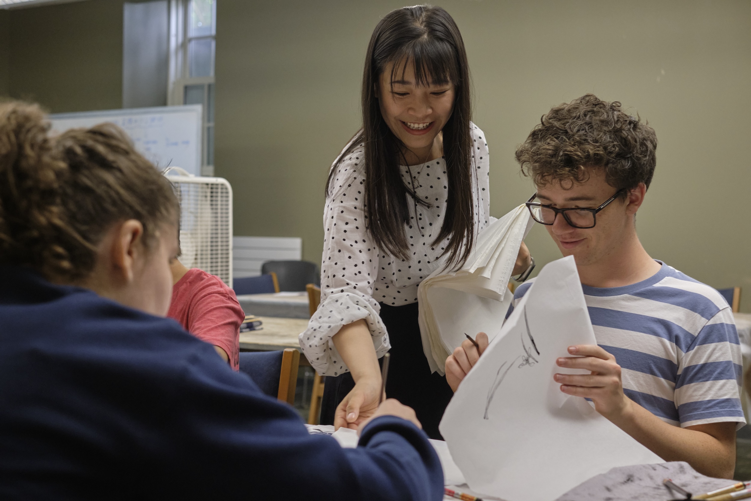 A woman helps a student with their Chinese calligraphy. 