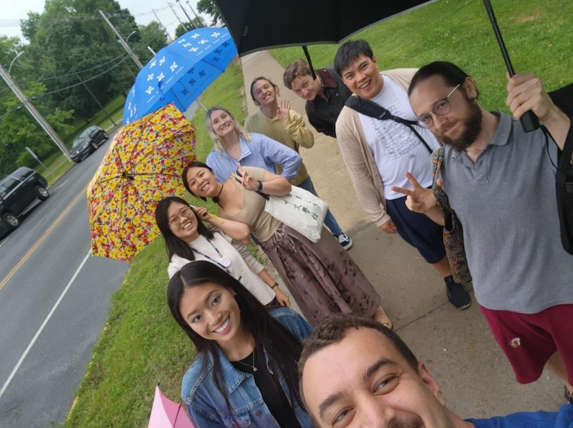 Chinese School students stand smiling under umbrellas on a rainy day. 