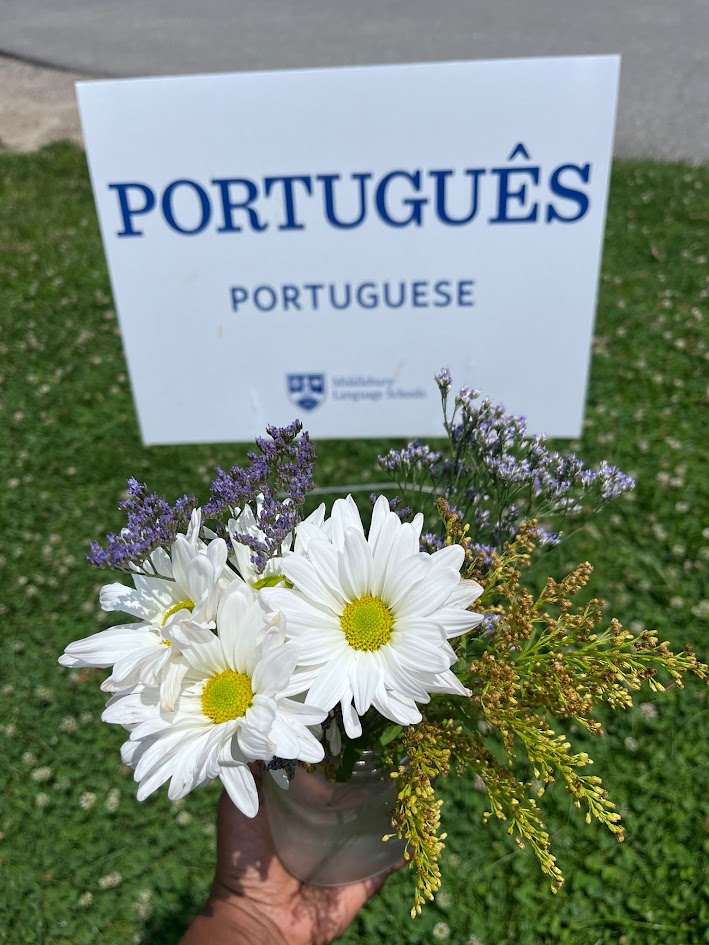 A sign that says "Português" and a person holding wildflowers in front of it. 