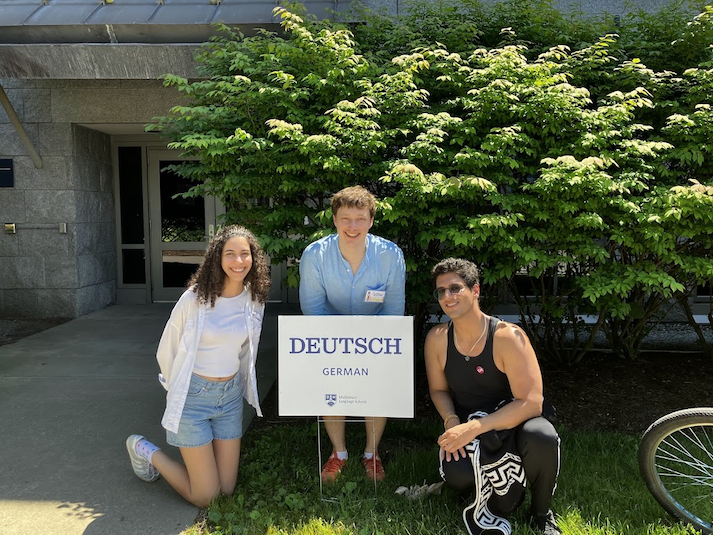 Three students smile behind the German School sign at Middlebury.