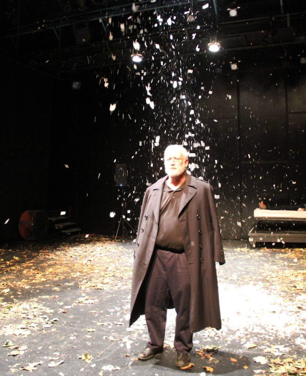 A man stands on stage with fake snow falling behind him. 