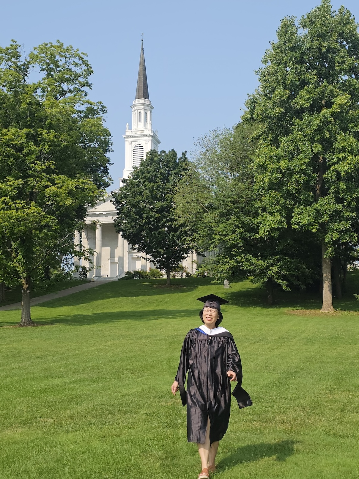 A woman in regalia walks across the Middlebury College lawn. 