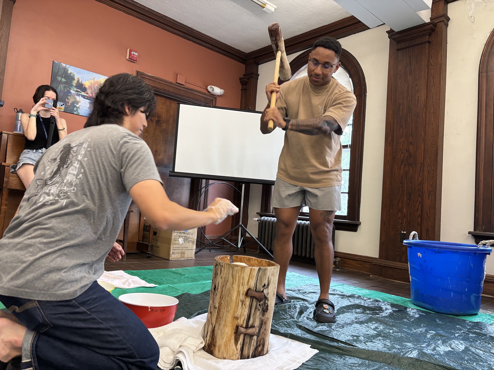 A man swings a wooden hammer down on a wooden stump. 