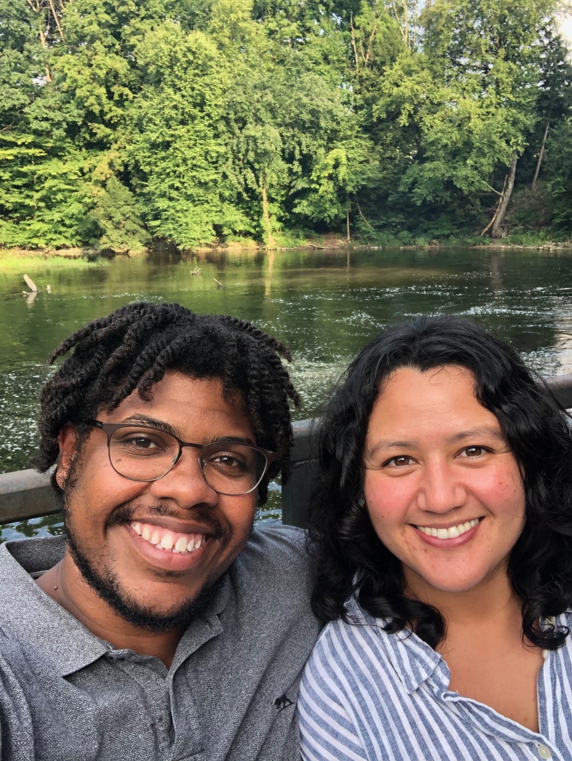 A woman and man smile while sitting beside a river. 