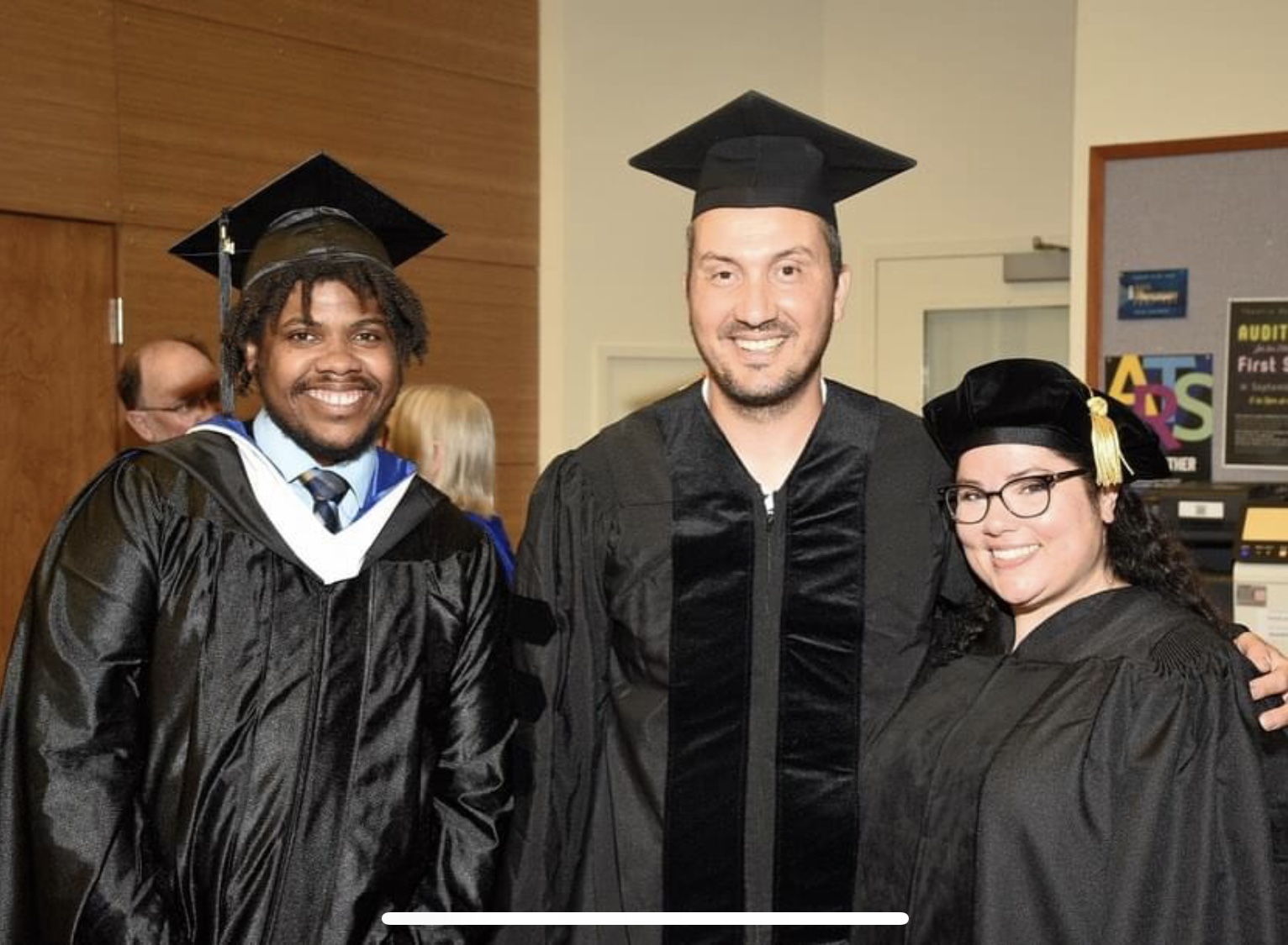 three graduate students smile in their regalia 