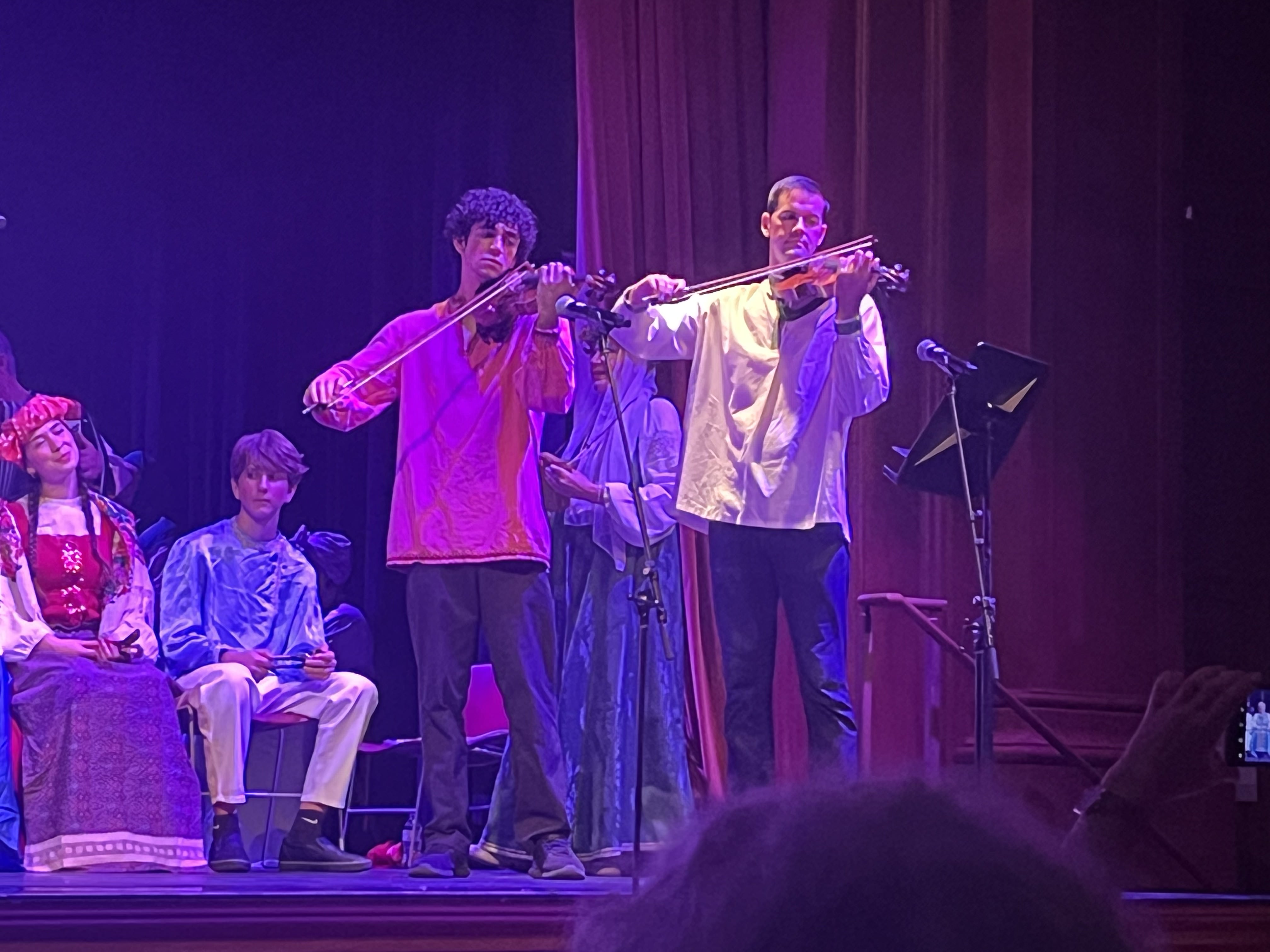 Two students play violin on a stage. 