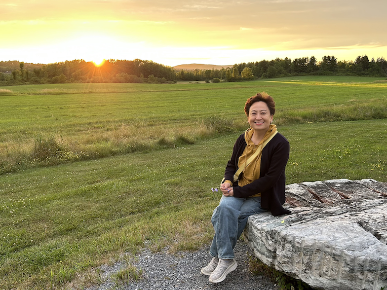 A woman in a black jacket and yellow scarf at sunset. 