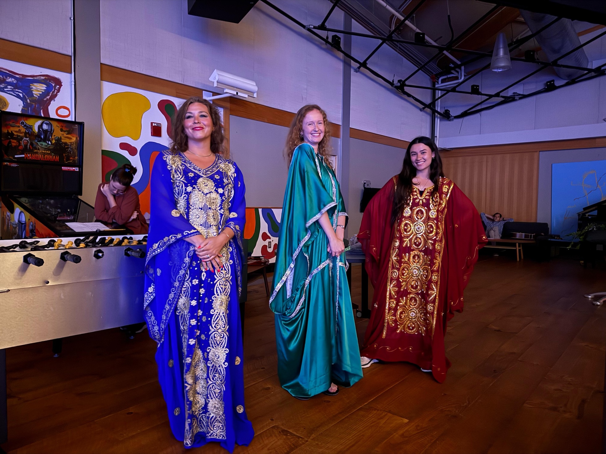 A group of three women in traditional Arabic dress clothes smile at the camera.