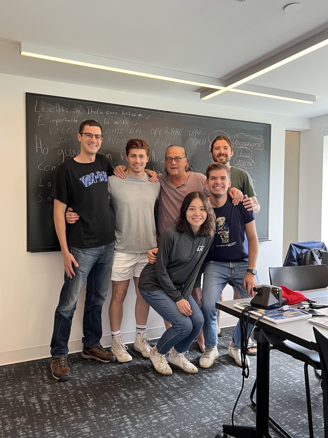 Students stand at the blackboard with their teacher, smiling. 