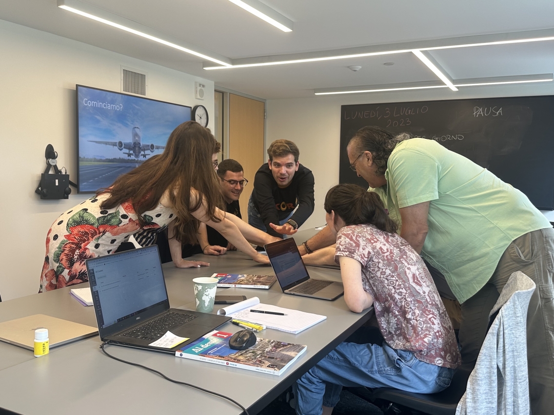 Students gather round to discuss something on a laptop. 