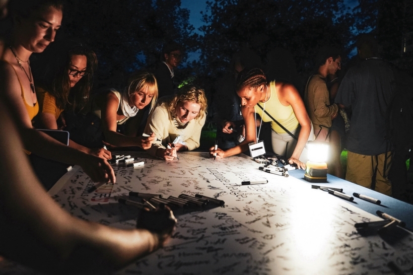 Students sign their names on a sign, lit by lanterns.
