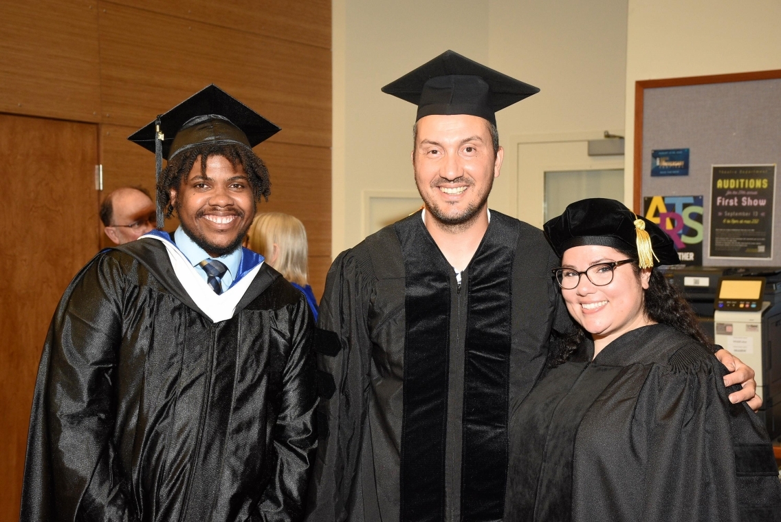 Three graduates stand together, smiling at the camera.