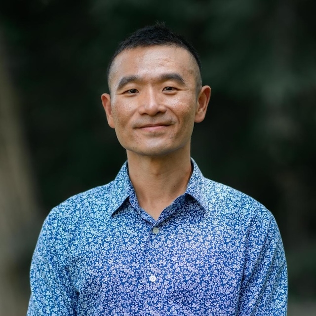 A man smiles in a blue shirt.