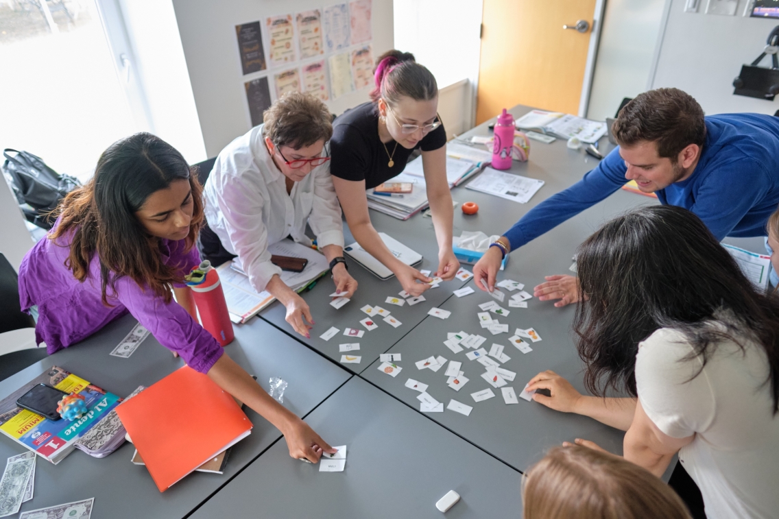 students work with their teacher at a table in Italian class.