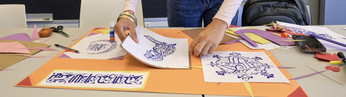 A woman displays her Arabic calligraphy on construction paper. 