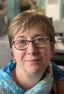 A woman in a blue scarf and glasses looks at the camera. 