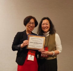 Two women smile at the camera holding an award