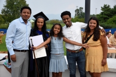 A family poses happily with their mother as she holds up her MA degree.