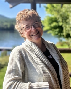 A woman smiles at the camera in front of a lake. 