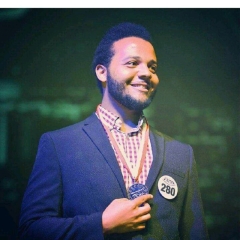 A man in a suit and medal smiles in front of a crowd.