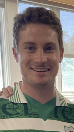 A man in a green and white striped shirt smiles at the camera 