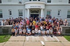 A group of students at the School of Japanese smiles at the camera in front of Hepburn Hall at Middlebury College. 