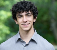 A man in a gray collared shirt smiles at the camera. 