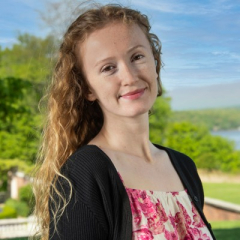 A woman in a red and white top and black cardigan smiles at the camera.