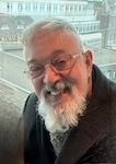 A man with white hair and glasses smiles at the camera. 
