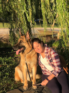 A woman in a plaid shirt smiles with her dog
