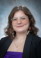 A woman in a black suit jacket smiles at the camera. 