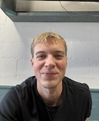 A man in a black t shirt smiles at the camera. 