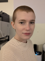 A woman in a tan sweater looks at the camera. 