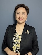 A woman in a black jacket and floral shirt smiles at the camera. 